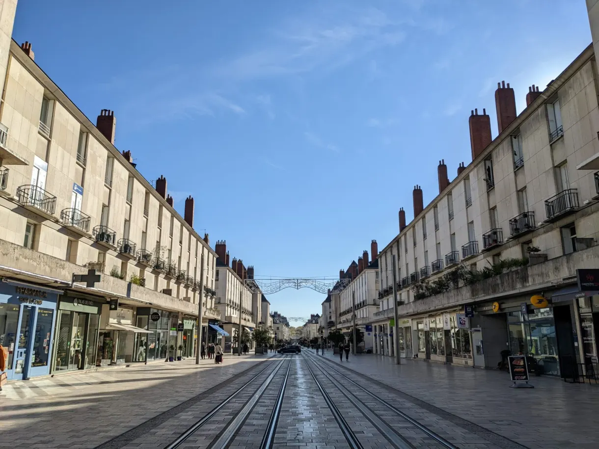 Rue commerçante rectiligne traversée par les rails du tramway