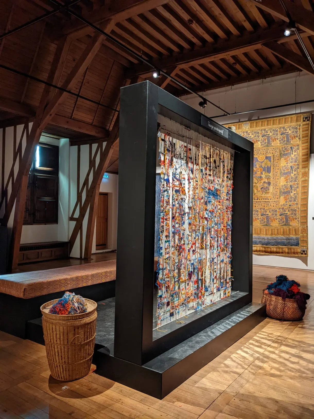 Grande tapisserie colorée exposée sous une charpente de bois