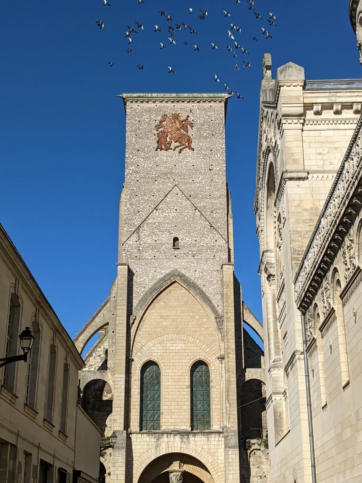 Tour carrée en pierre survolée par une nuée d'oiseaux