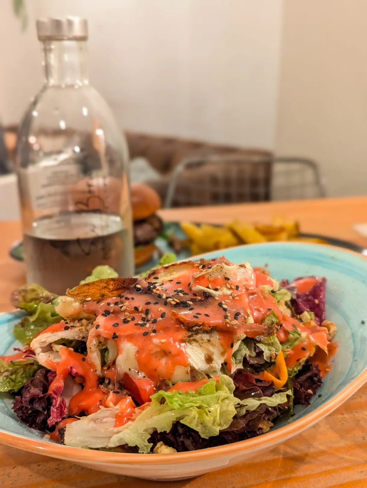 Grande salade nappée de sauce, carafe de vin derrière