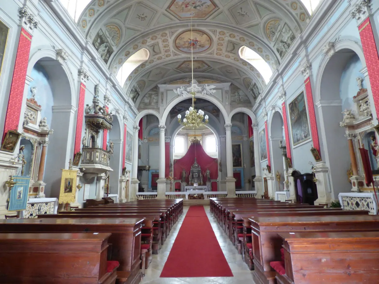 Nef baroque au tapis rouge et bancs de bois dans une église de Buje