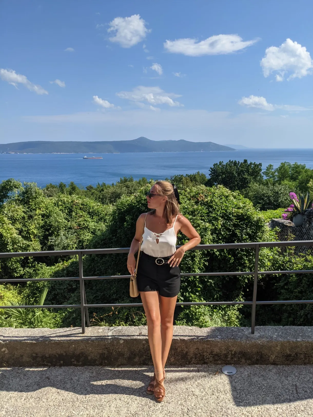 Femme accoudée à une rambarde face à la mer et aux reliefs du large