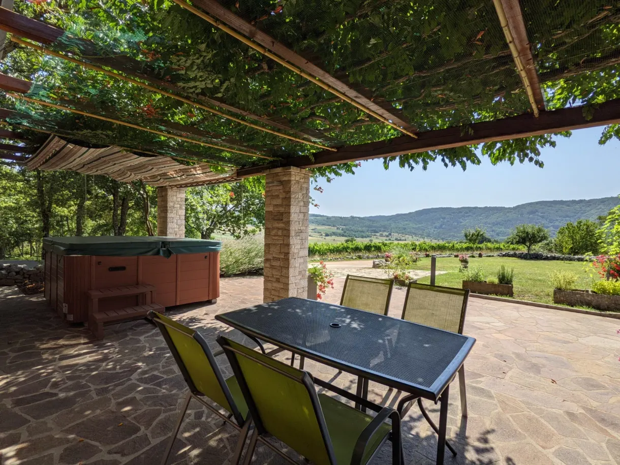 Table et chaises sous la pergola de la terrasse, bain à remous au fond