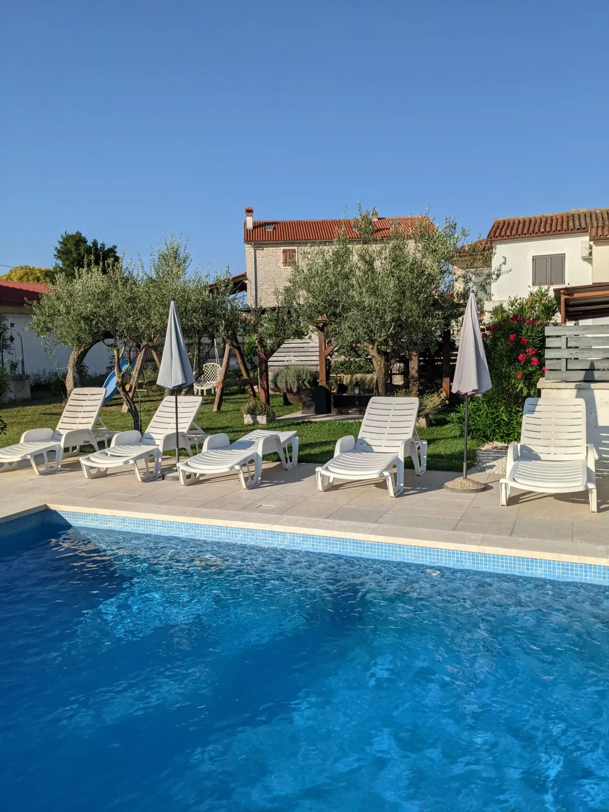 Piscine bordée de transats et de parasols devant la maison de vacances