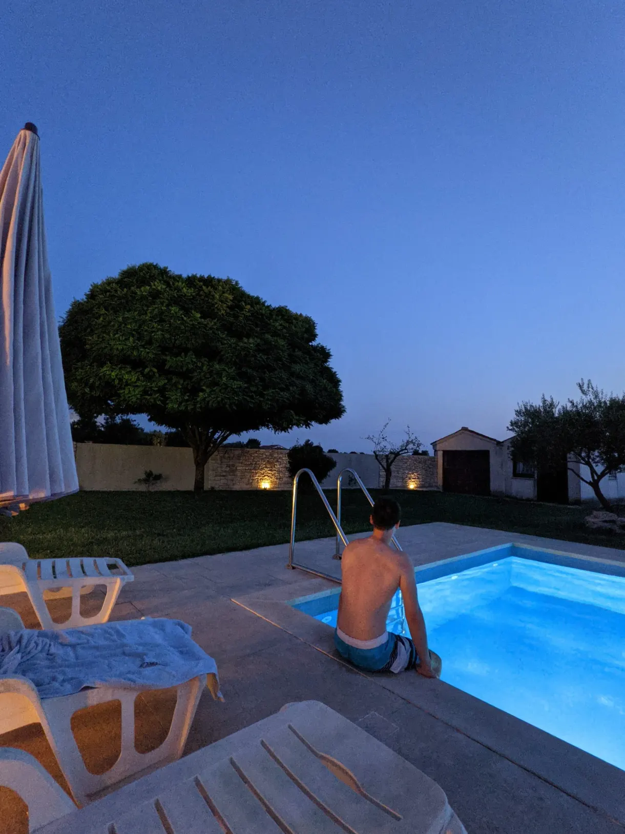 Piscine éclairée à la nuit tombée sous un grand arbre