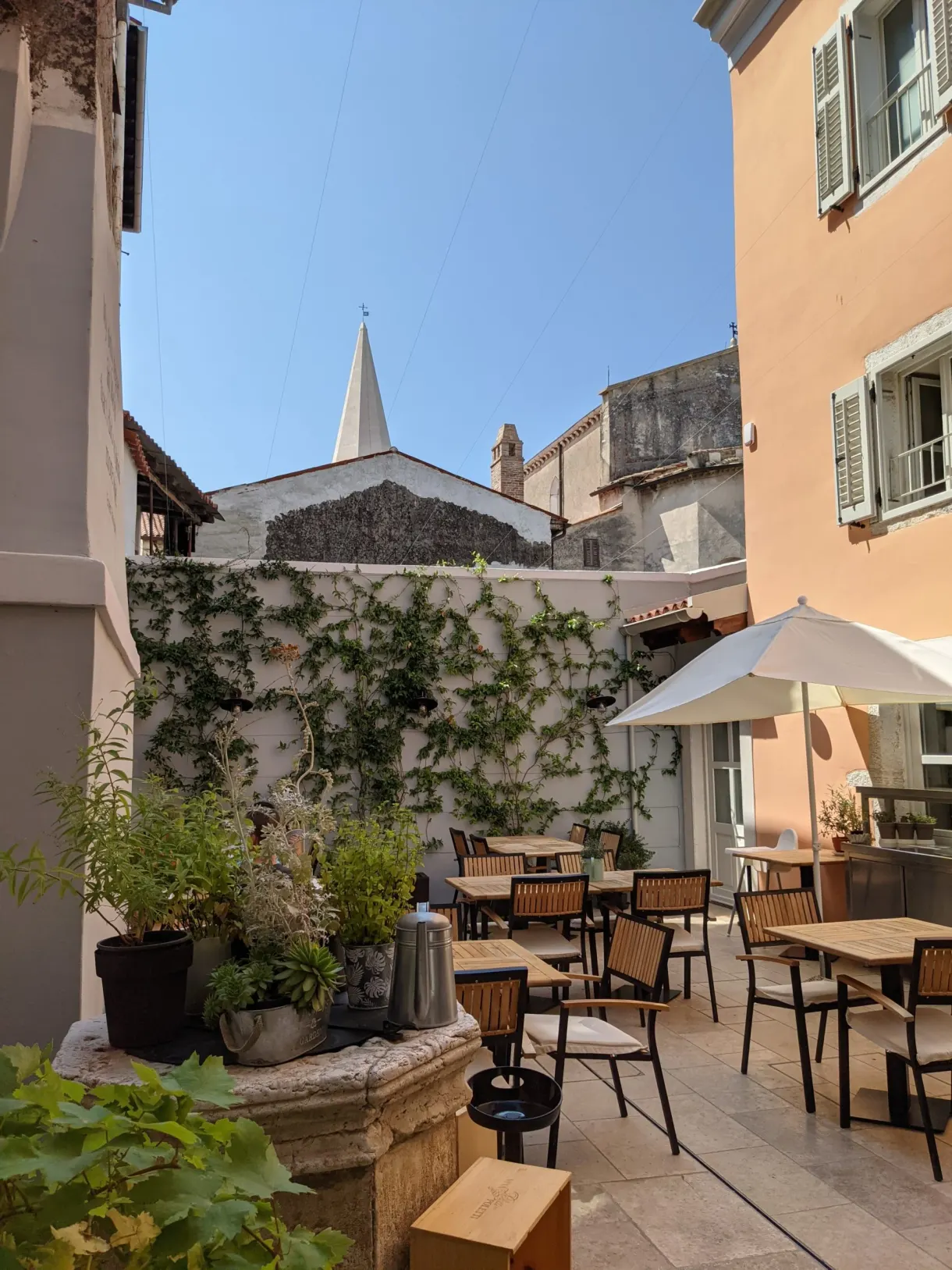 Cour de restaurant aux tables dressées et parasol, clocher en arrière-plan