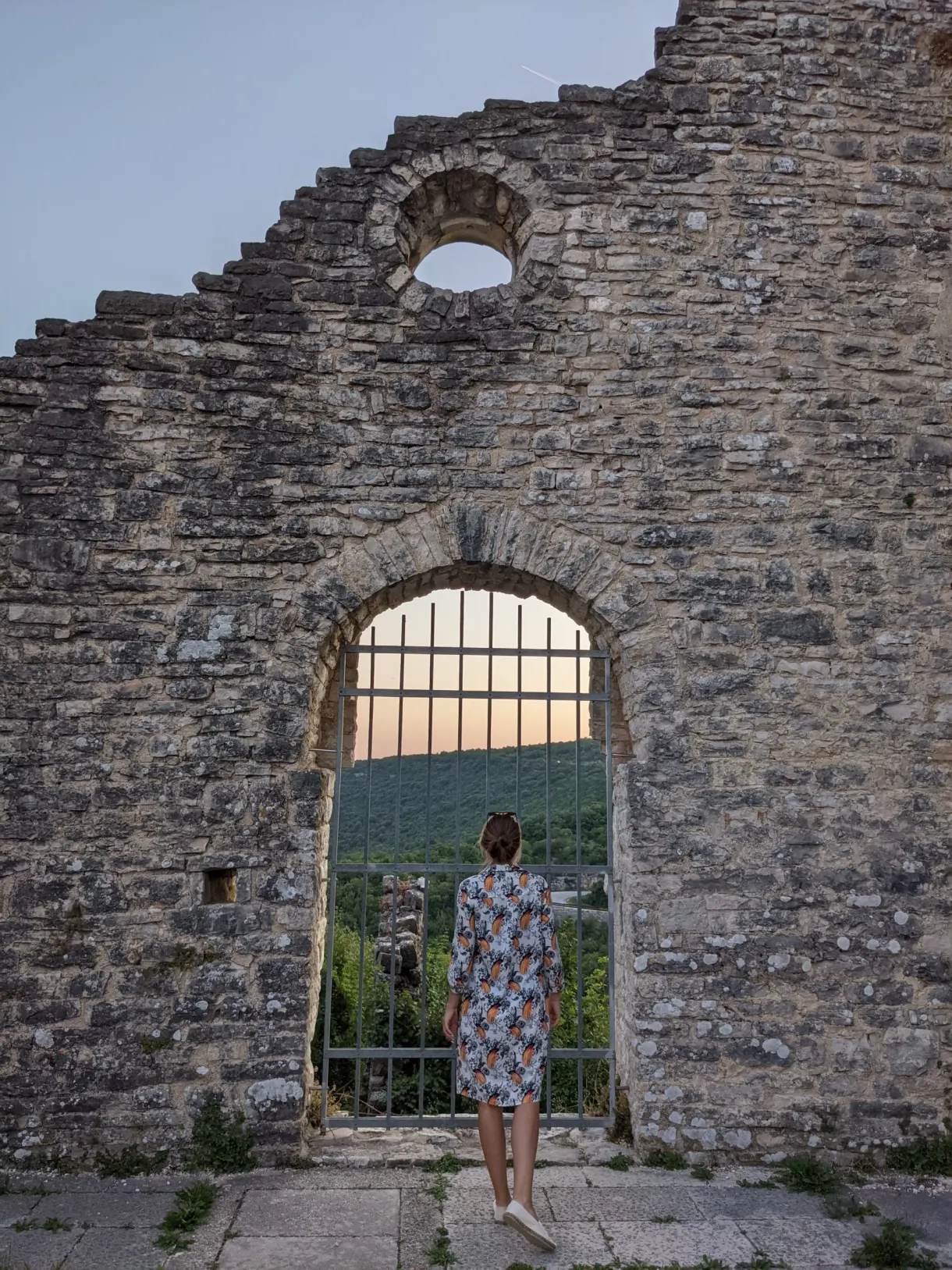 Femme devant la haute baie grillagée d'une église en ruine de Dvigrad