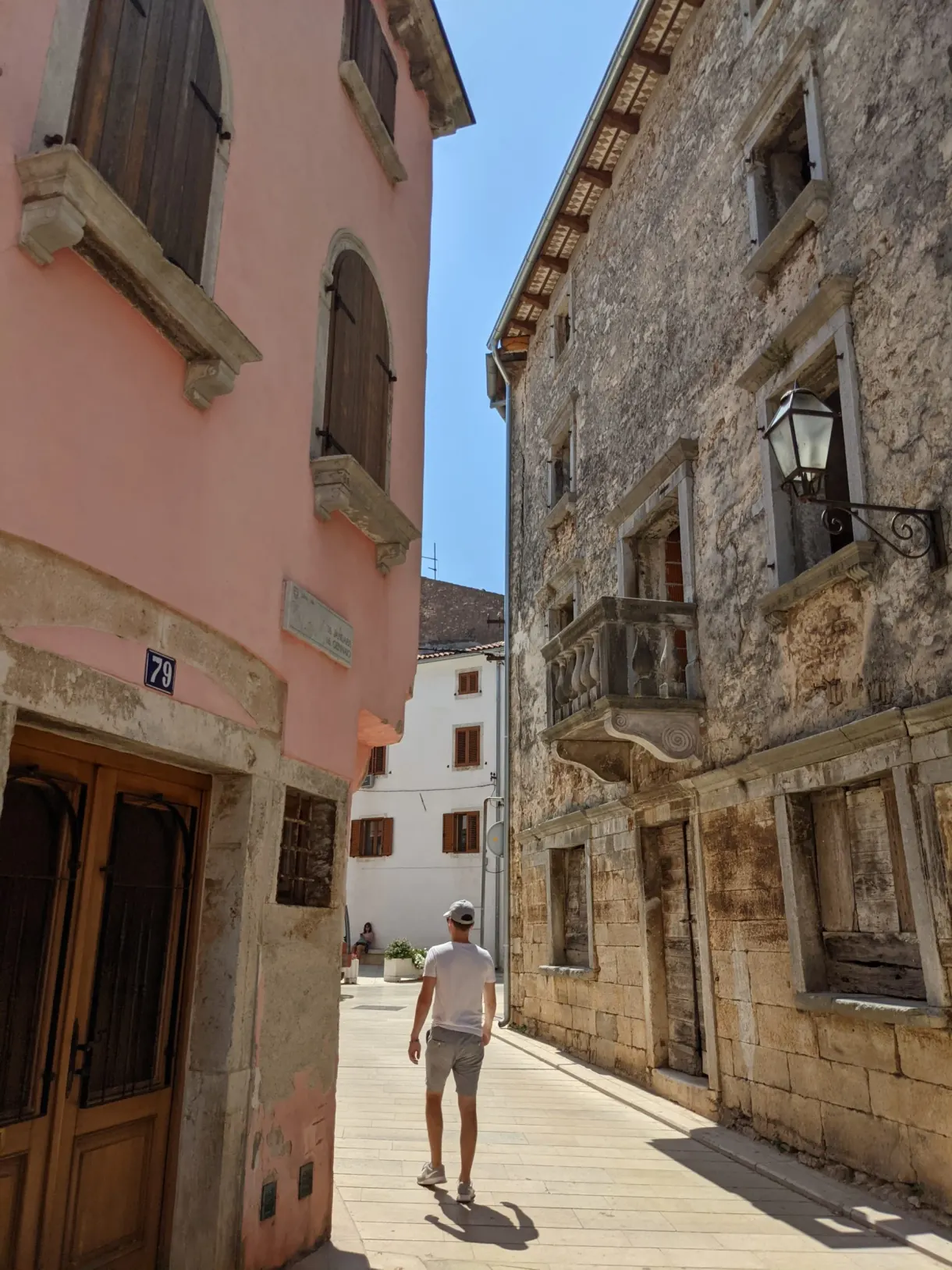 Passant dans une rue de Vodnjan entre façade rose et mur de pierre