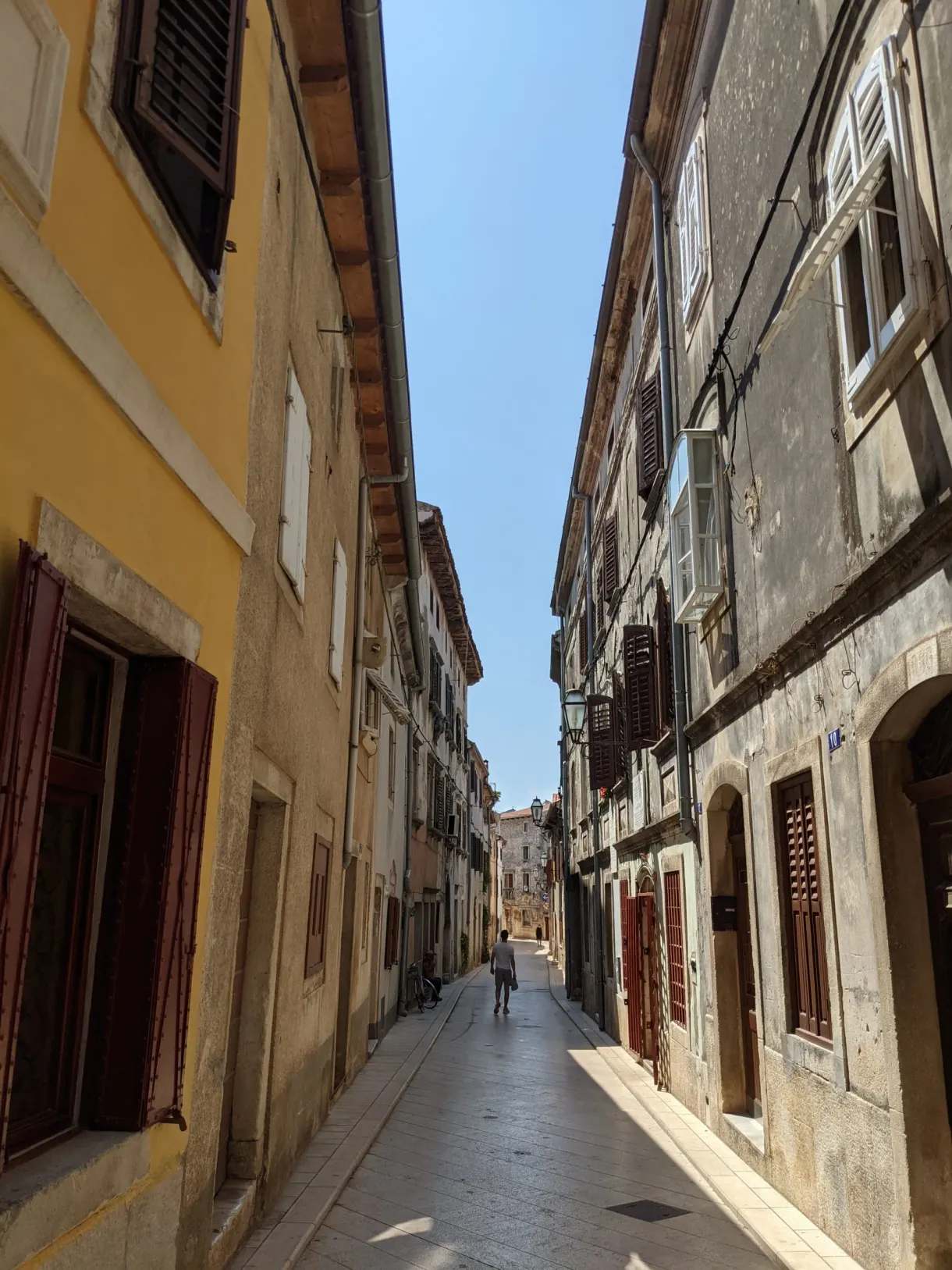 Rue étroite entre une maison jaune et des façades de pierre, Vodnjan
