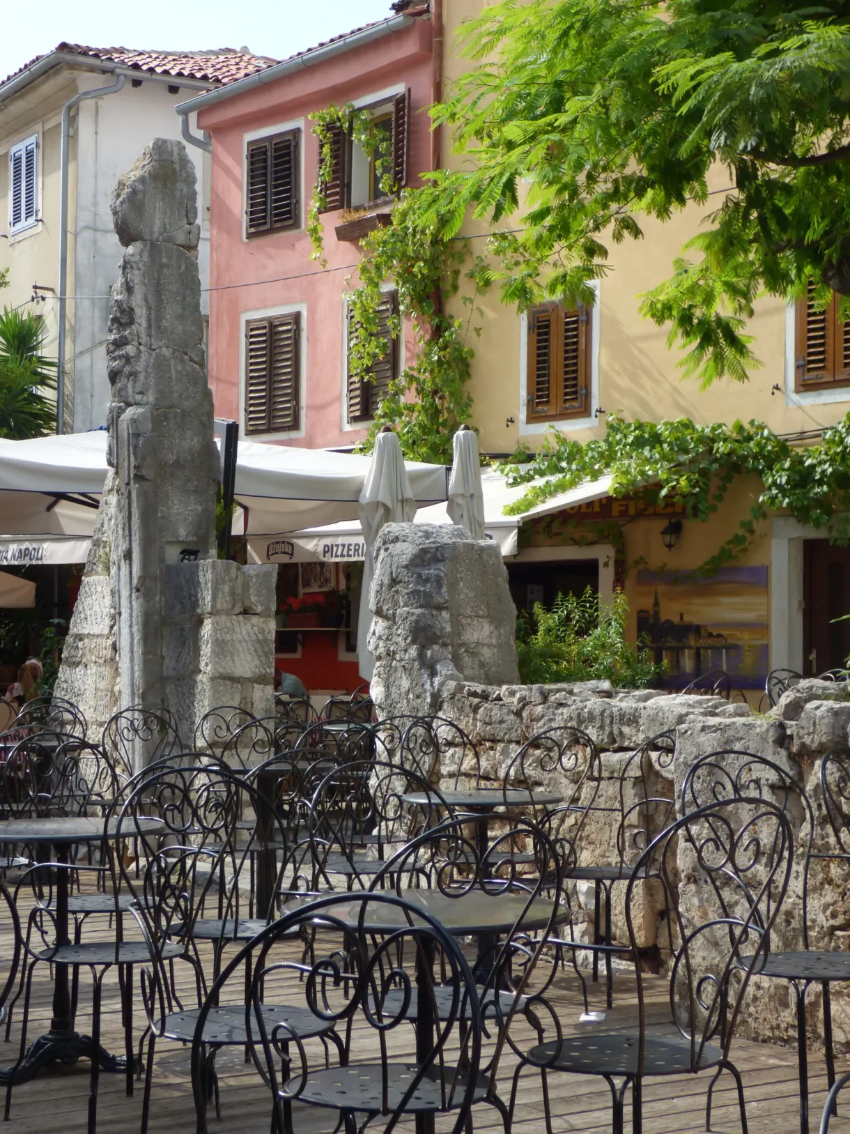 Chaises en fer forgé d'un café entre des fûts de colonnes antiques, Poreč