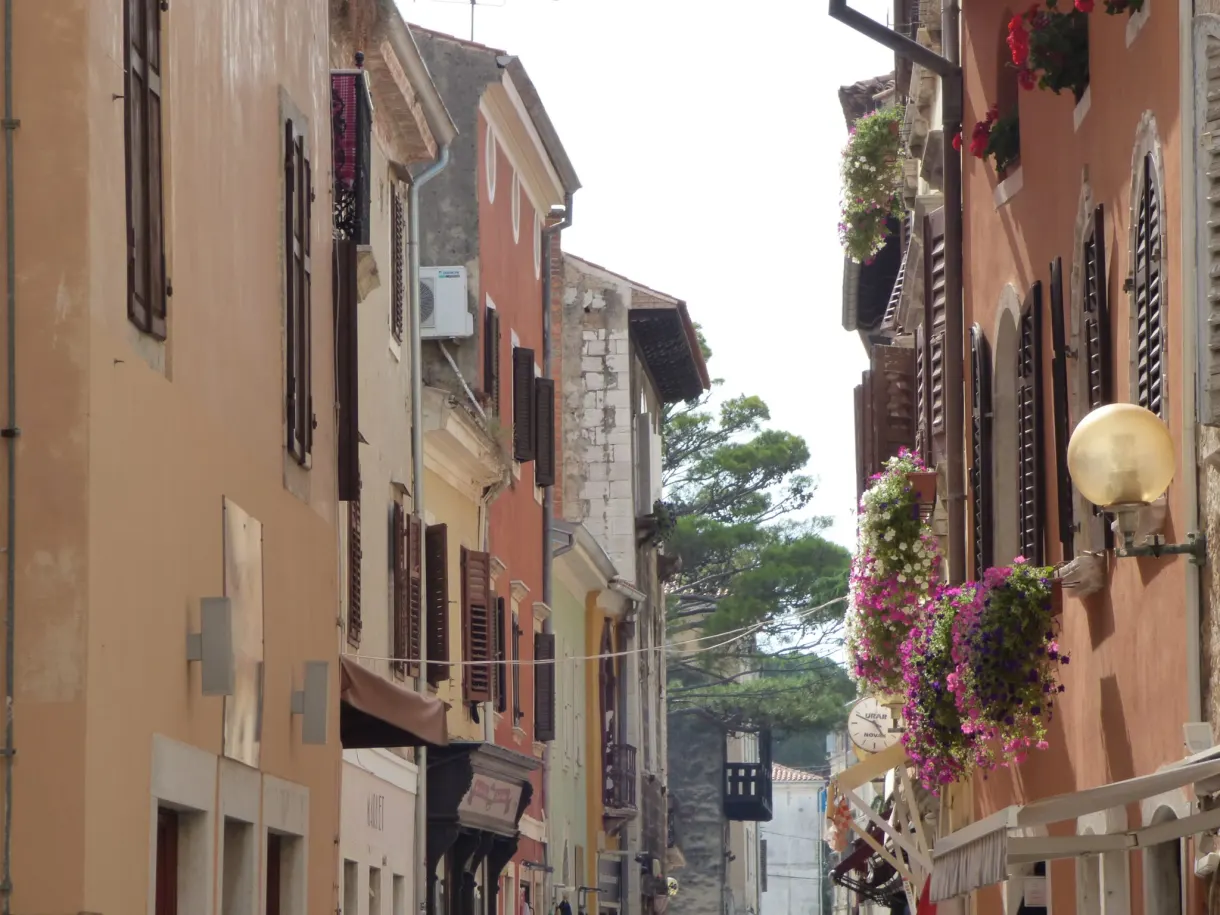 Façades pastel et paniers de fleurs suspendus dans une rue de Poreč