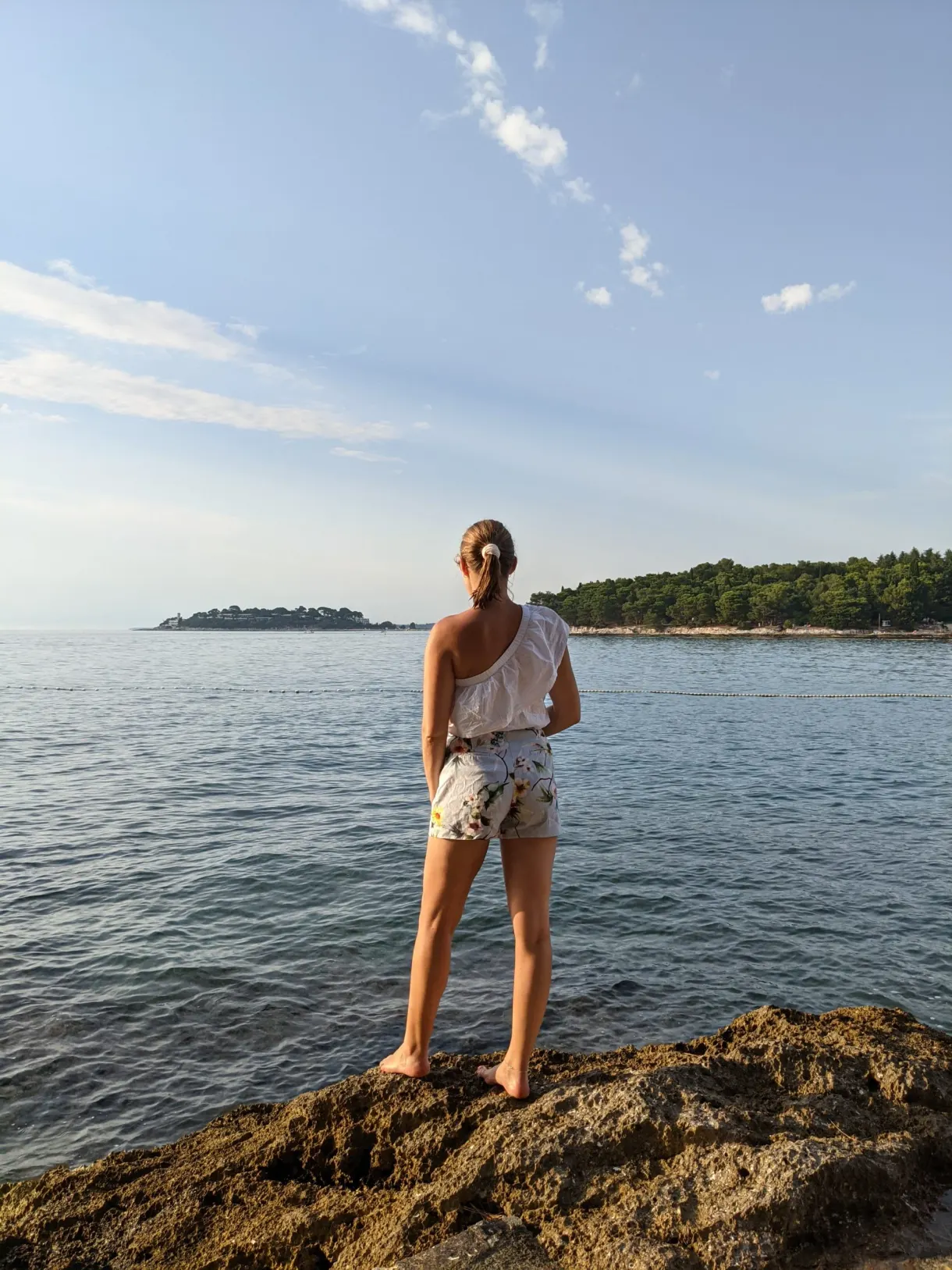 Femme debout sur un rocher face à un îlot boisé de la Plava Laguna
