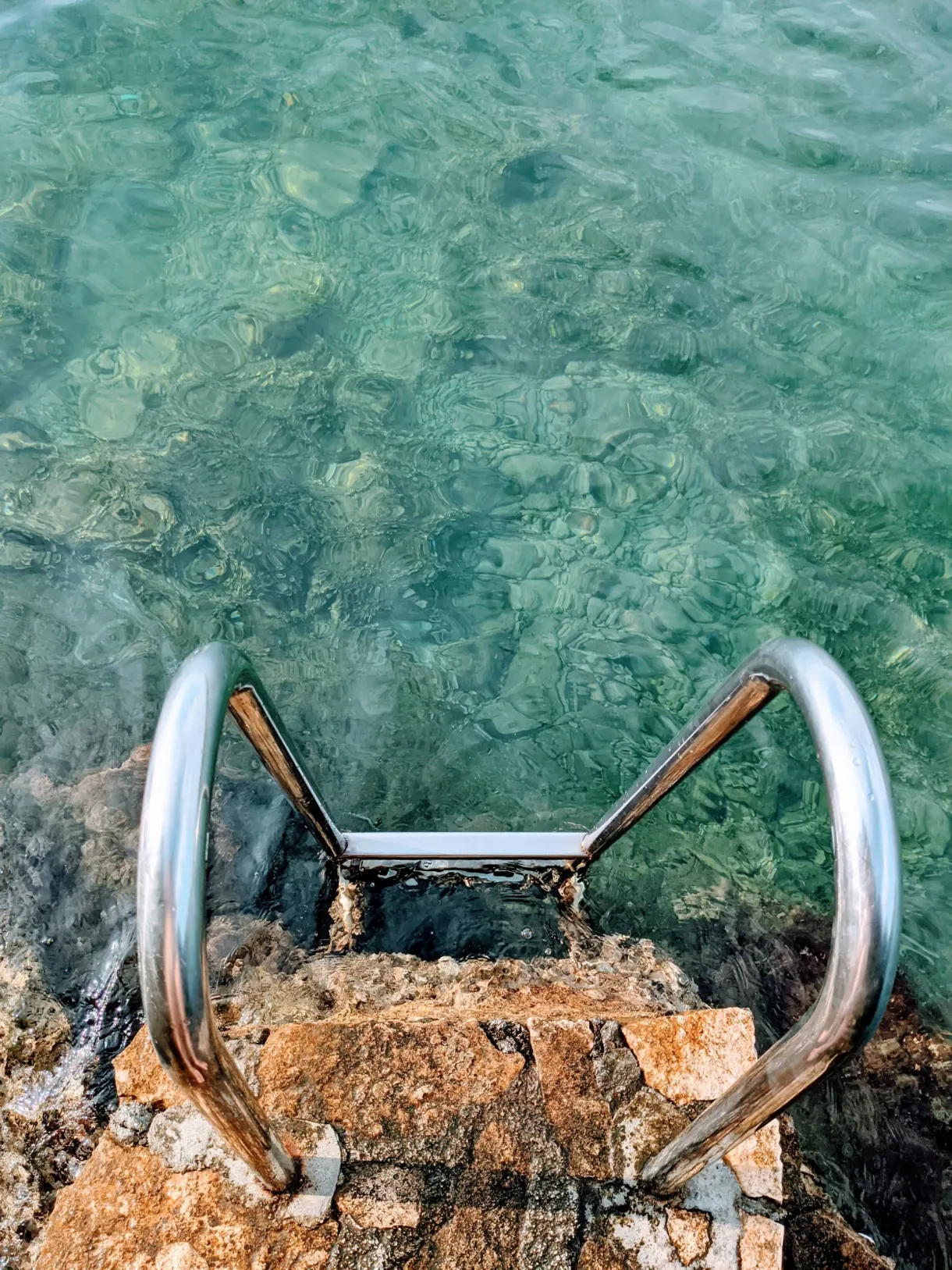 Échelle de baignade en inox scellée dans un rocher, eau turquoise