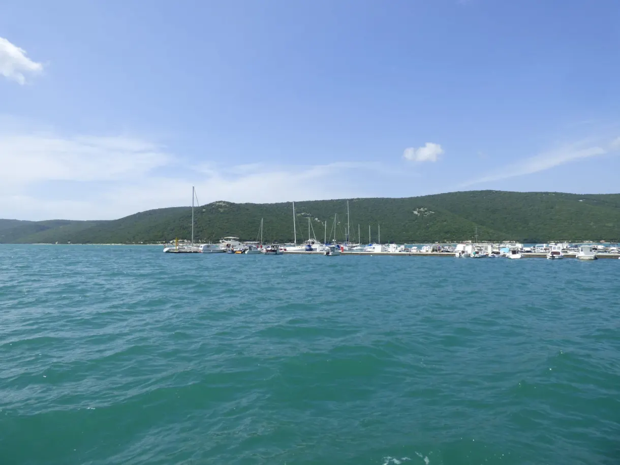 Mâts de voiliers et eau turquoise devant les collines de Trget
