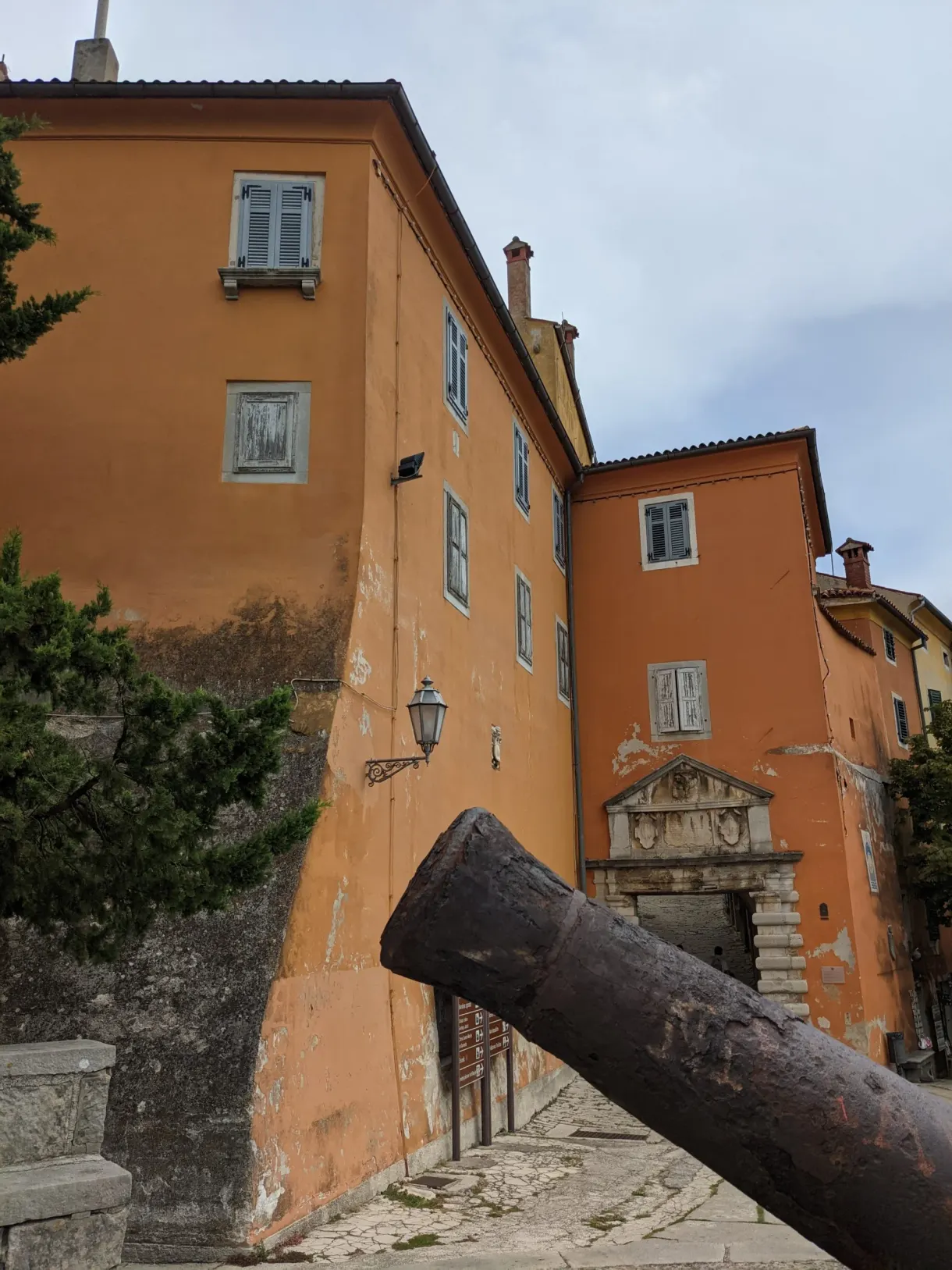 Canon couché devant une façade orange de la vieille ville de Labin