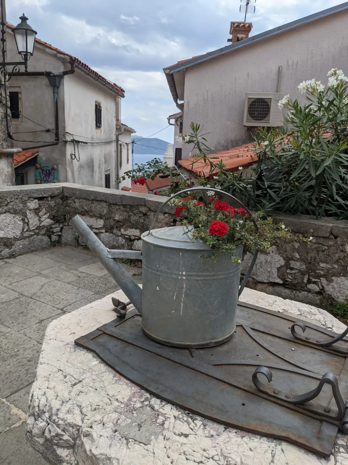 Arrosoir en zinc fleuri posé sur un muret du village de Brseč
