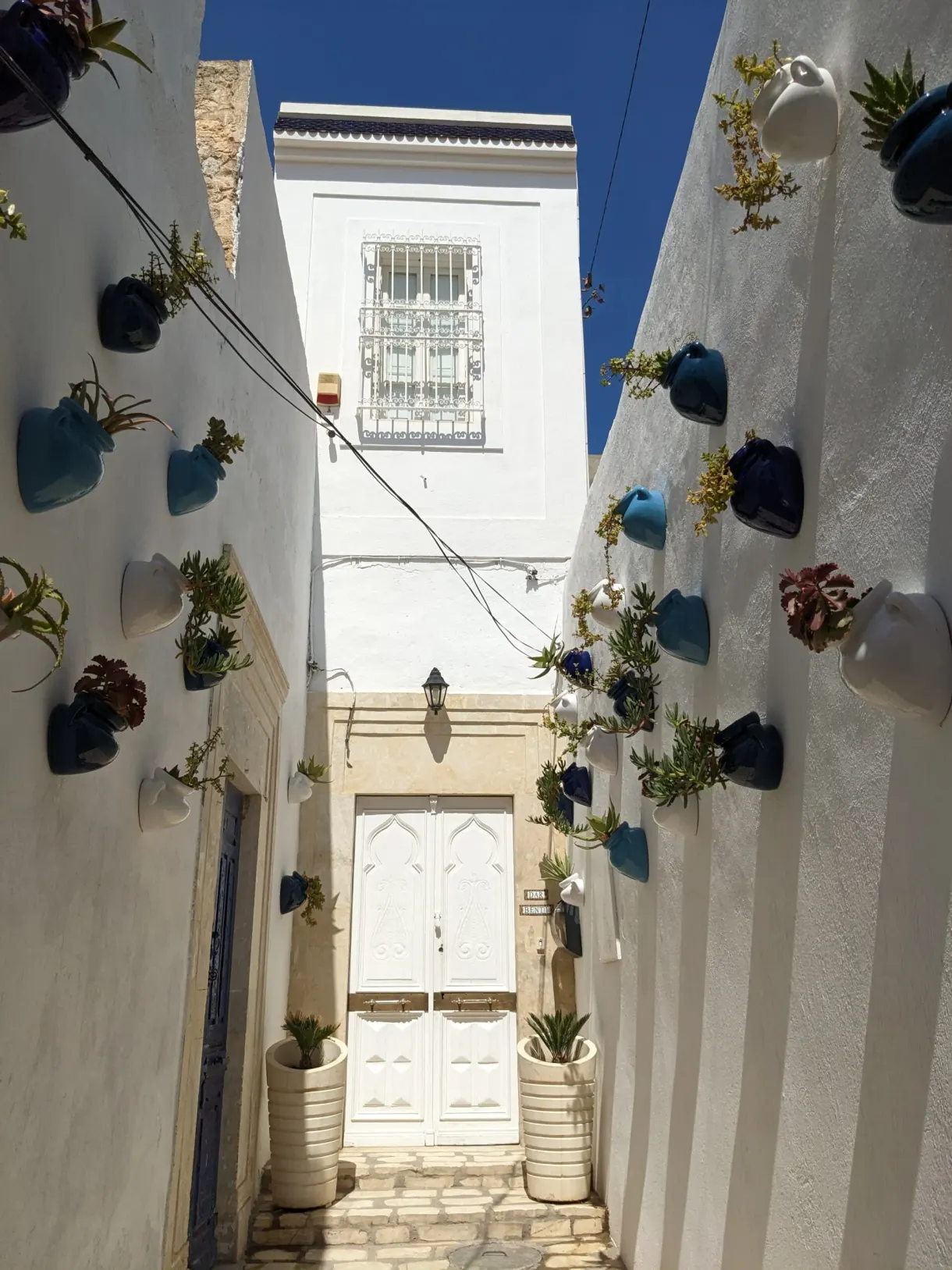 Ruelle blanche de la médina de Monastir ornée de pots bleus, devant la maison d'hôtes Dar Benti