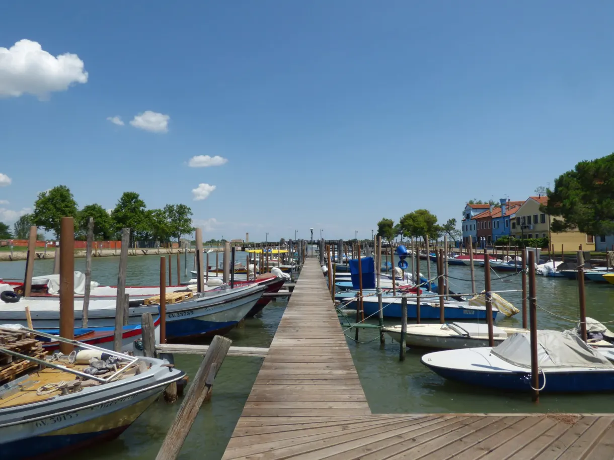 Wooden pontoon between moored boats facing the colourful houses