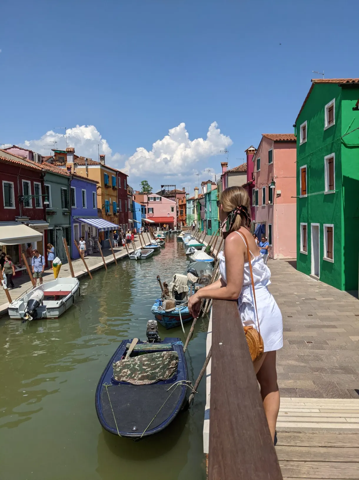 Leaning on the railing facing the canal and a covered boat