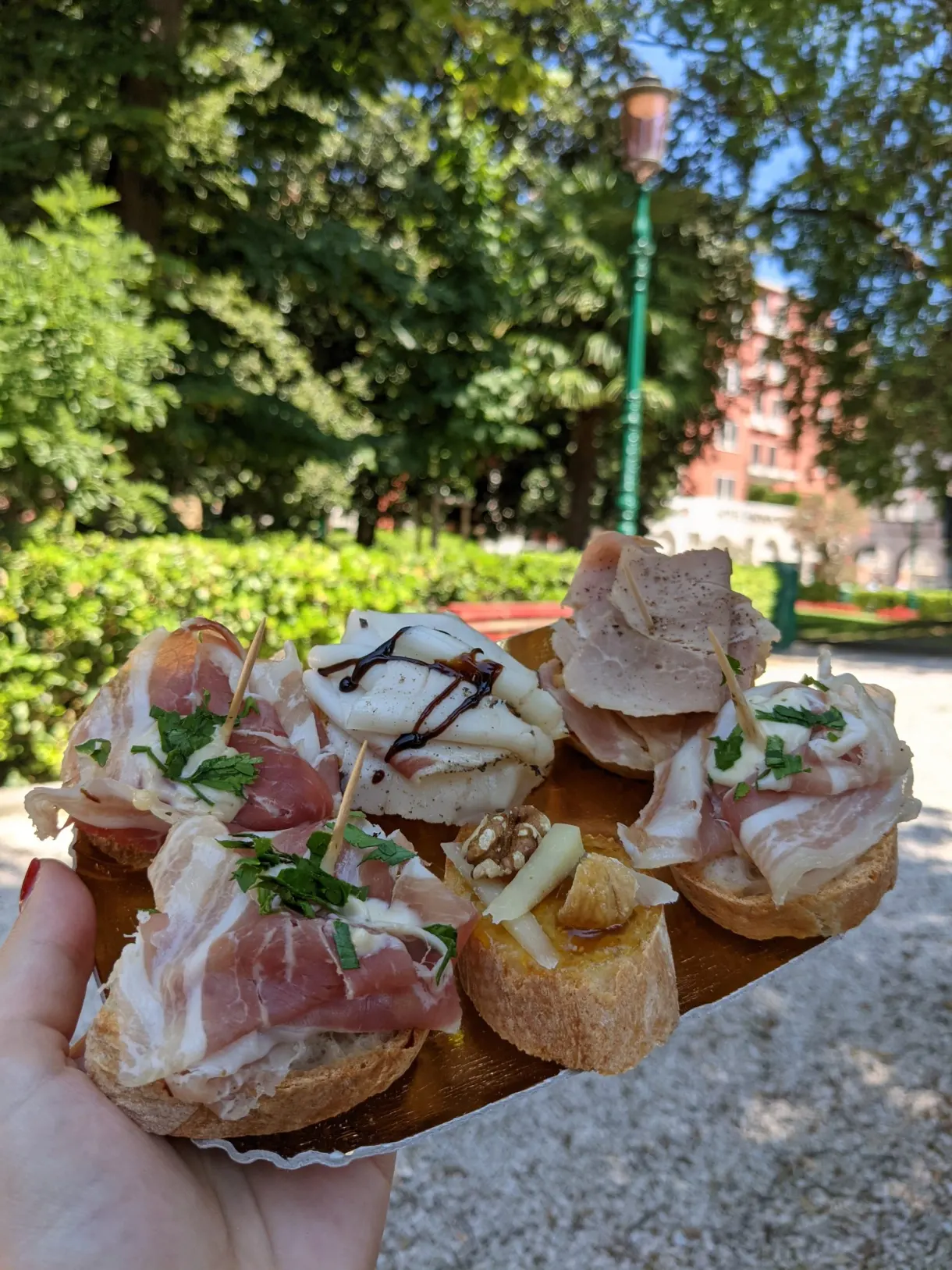 Hand holding cicchetti topped with charcuterie and cream