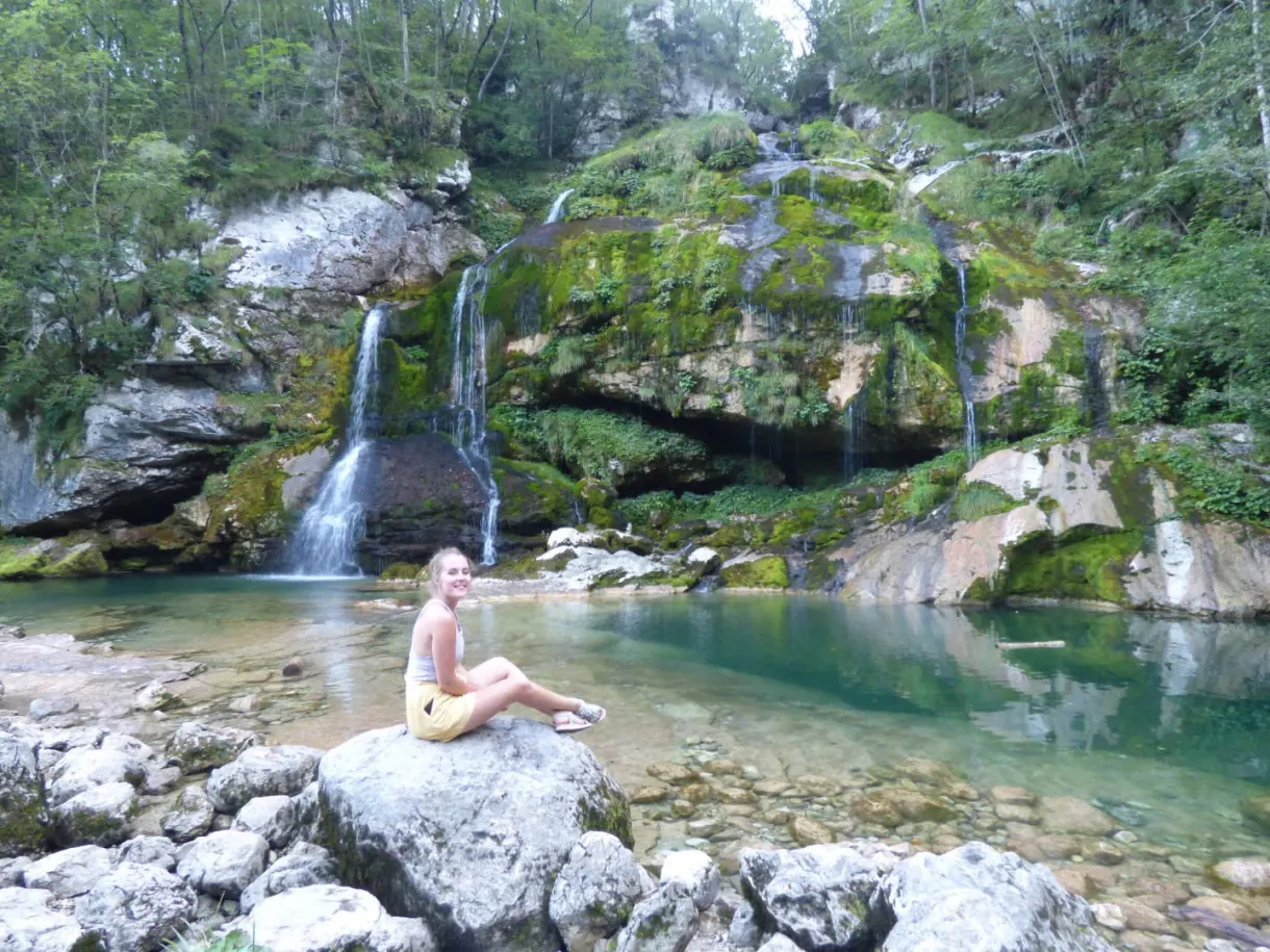 Assise sur un rocher devant la cascade et son bassin turquoise