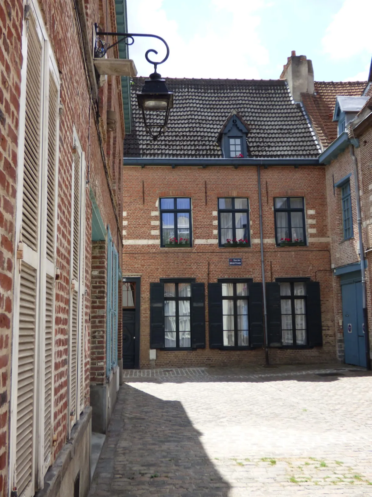 Petite place pavée bordée de maisons de brique à volets noirs
