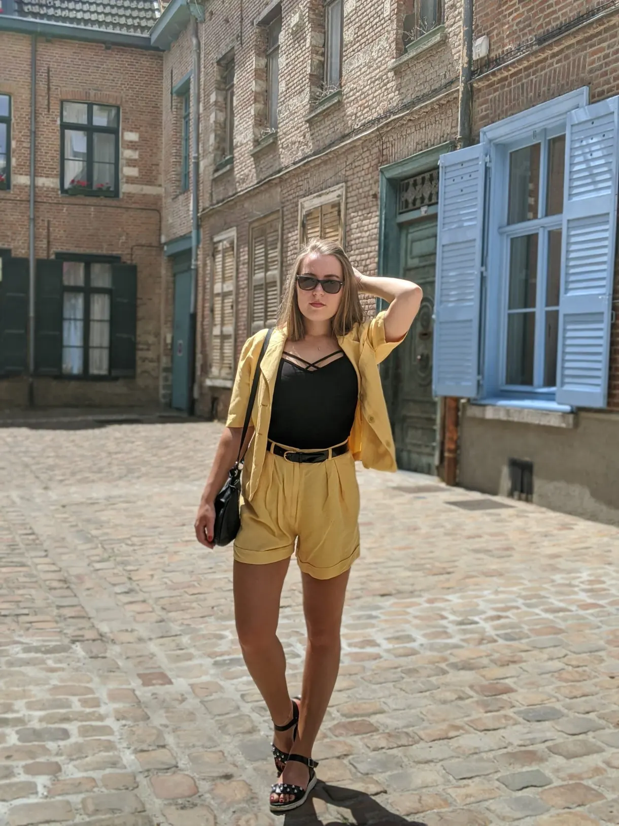 Femme en tenue jaune sur les pavés devant des volets bleus