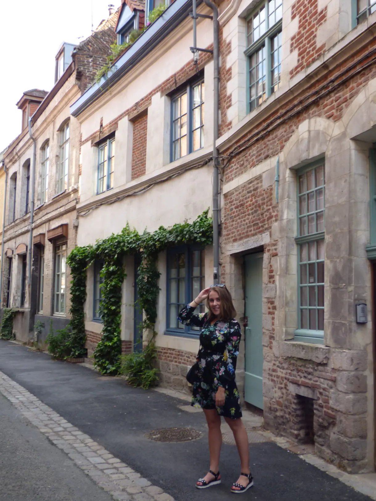 Femme en robe fleurie dans une ruelle tapissée de lierre