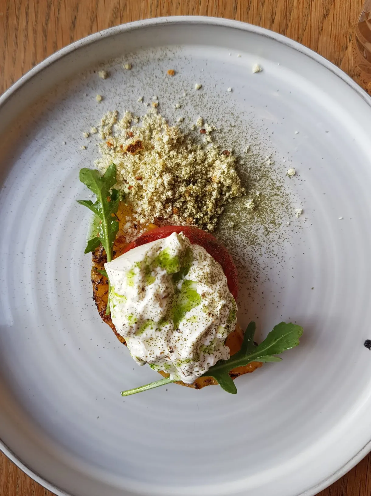 Burrata et crumble vert dressés dans une assiette blanche