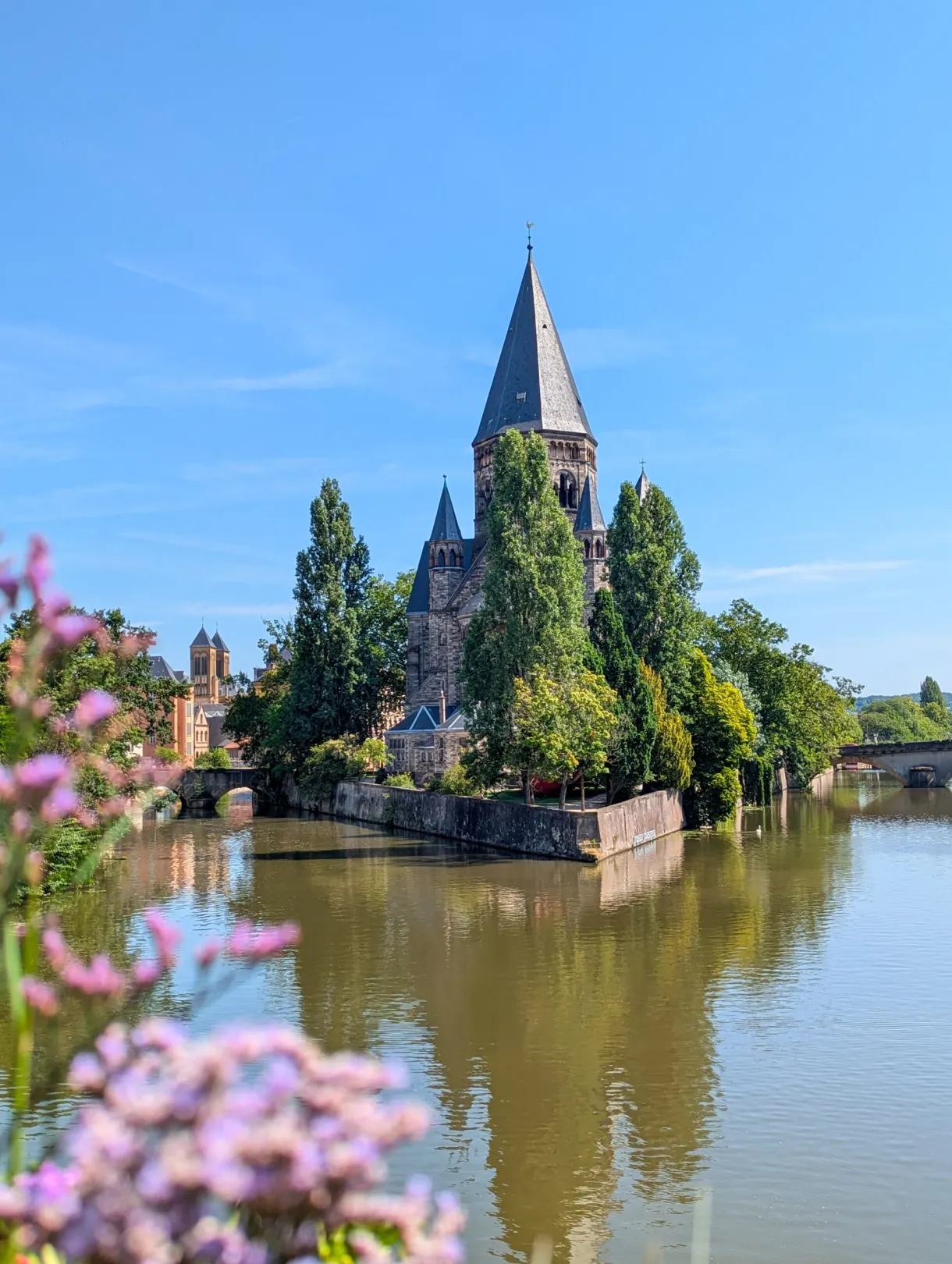 Église au clocher pointu entourée d'arbres, reflétée dans l'eau verte