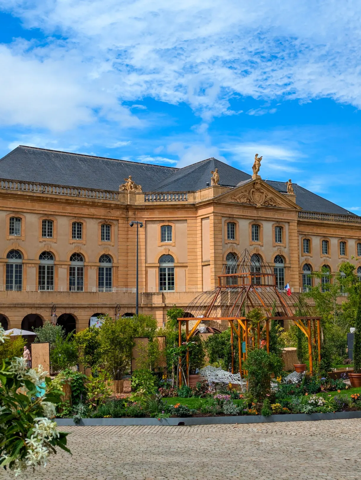 Façade classique en pierre dorée devant un jardin éphémère et sa pergola