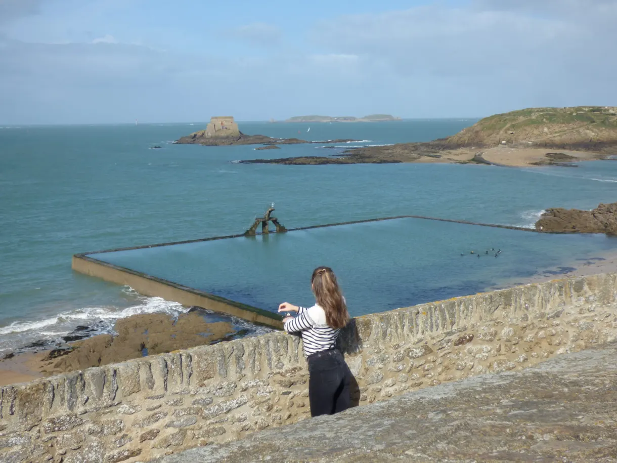 Promeneuse accoudée au rempart devant la piscine de mer