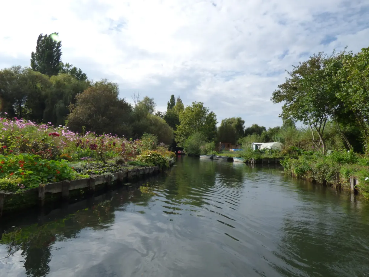 Large canal bordé de jardins flottants sous un ciel nuageux