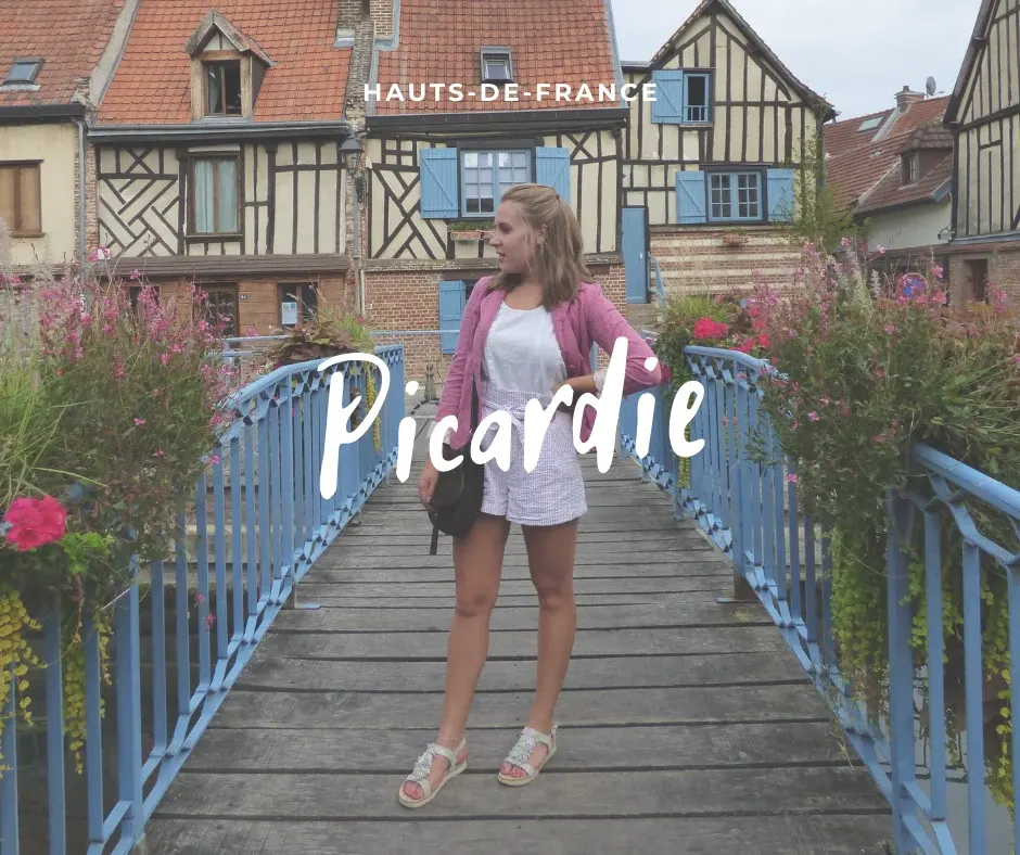 Voyageuse sur une passerelle bleue fleurie devant des maisons à colombages