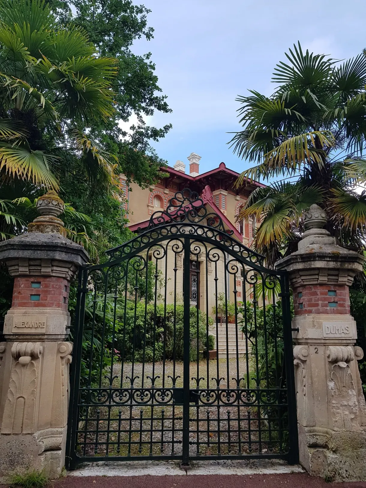Portail en fer forgé encadré de palmiers devant une villa