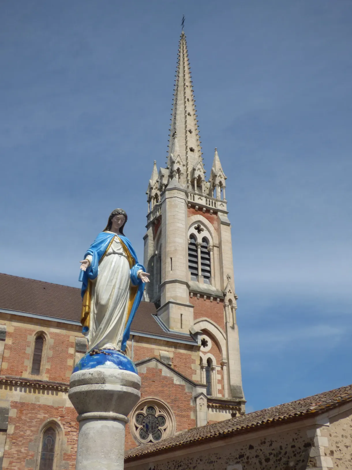 Statue de la Vierge devant le clocher de brique de l'église