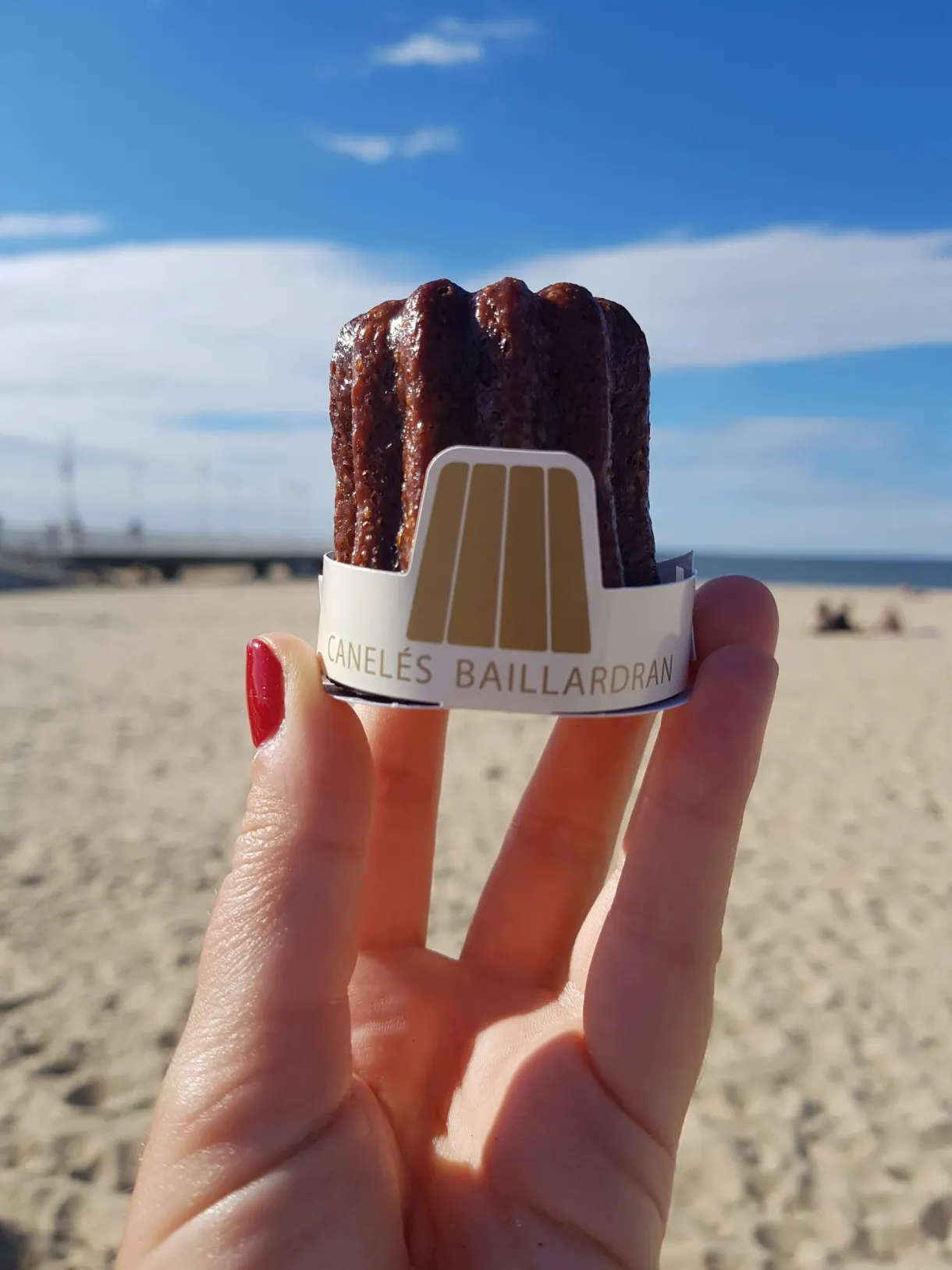 Cannelés bordelais tenus à la main devant la plage