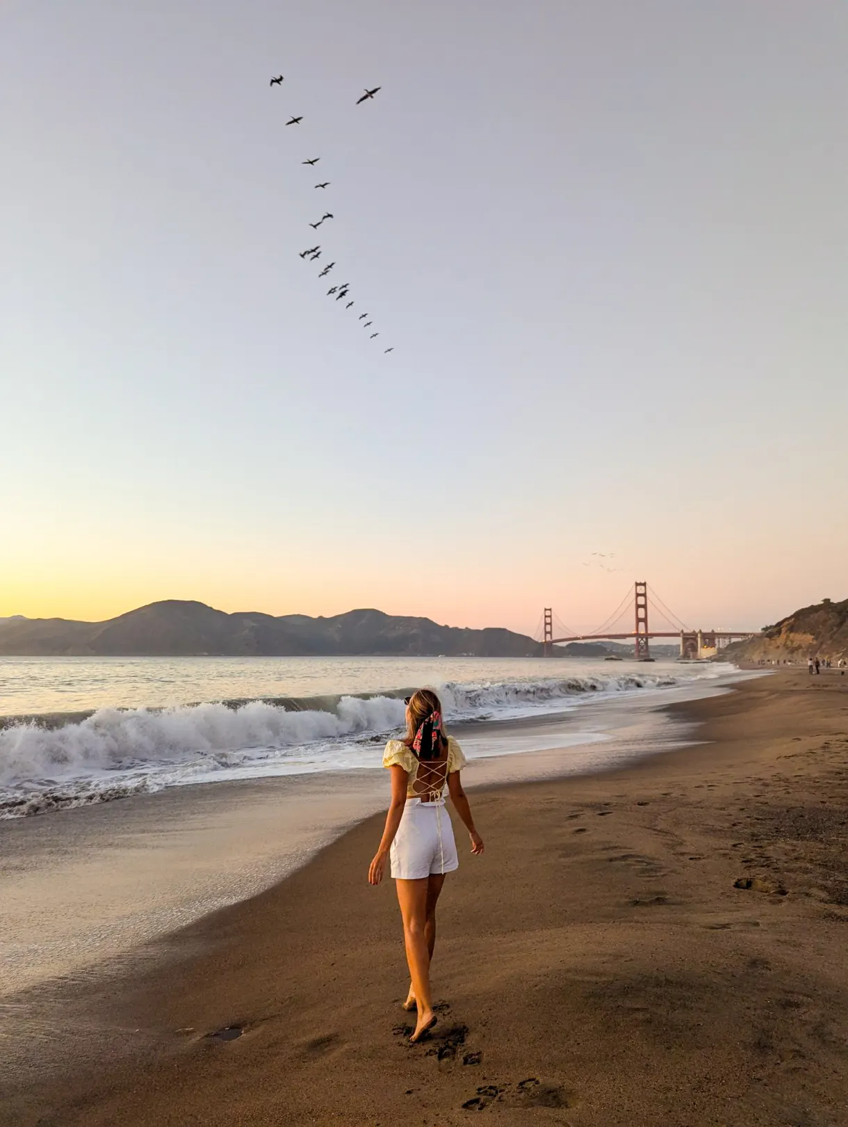 fille sur une plage la tête vers le ciel avec le pont de san francisco en arrière-plan